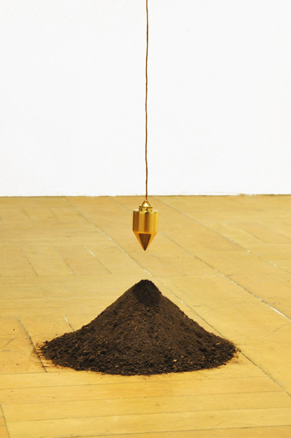 Escultura A Gênese (2011) de Felippe Moraes com prumo banhado a ouro suspenso acima de um montículo de terra