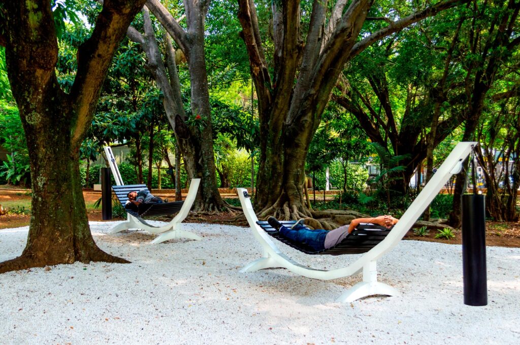 Série Composição Aleatória, 2019 metal escovado, madeira, chapa de aço pintada e cabo de aço 165 x 395 x 96 cm A obra “Composição Aleatória” (2019) foi concebida, construída e instalada pela primeira vez nesta exposição. Oito redes – correspondentes às sete notas musicais acrescidas do Dó da oitava acima – estão presas a tubos sonoros e badalos que vibram e ecoam dependendo dos movimentos a que são submetidos. Nossos corpos são novamente convidados a participar da criação do trabalho, ativando os balanços e ressoando os sinos. A composição cresce e se complexifica à medida que mais pessoas juntam-se à instalação, até que todos os sons sejam entoados em harmonia ou dissonância. Em momentos distintos, composições diferentes preenchem o espaço expositivo – os arranjos dependem, sempre, dos arbitrários e aleatórios gestos dos visitantes, que podem embalar-se com intensidade ou apenas recostar-se em meio à melodia improvisada.