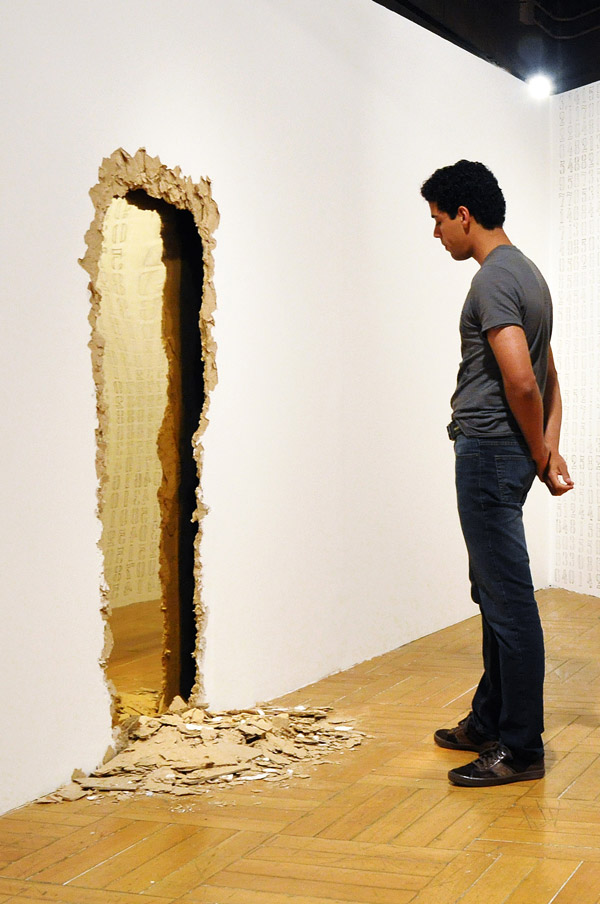 Obra Entranha de Felippe Moraes com abertura em parede de drywall revelando interior dourado em latão polido