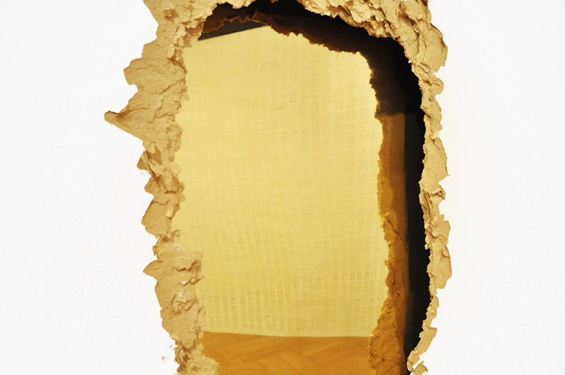 Obra Entranha de Felippe Moraes com abertura em parede de drywall revelando interior dourado em latão polido