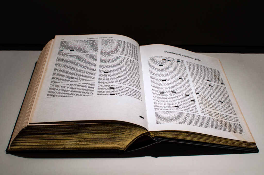 Detalhe da página de Bíblia com palavra “Deus” removida na obra Verbo de Felippe Moraes.