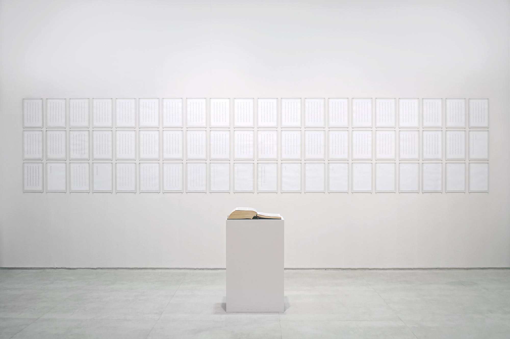 Vista geral da instalação Verbo com Bíblia recortada e palavras “Deus” organizadas em folhas de papel.